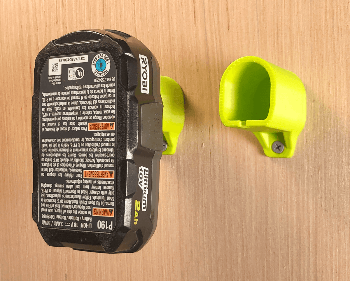 Ryobi battery stored in a green wall mount beside an empty green mount; battery and hardware are not included.