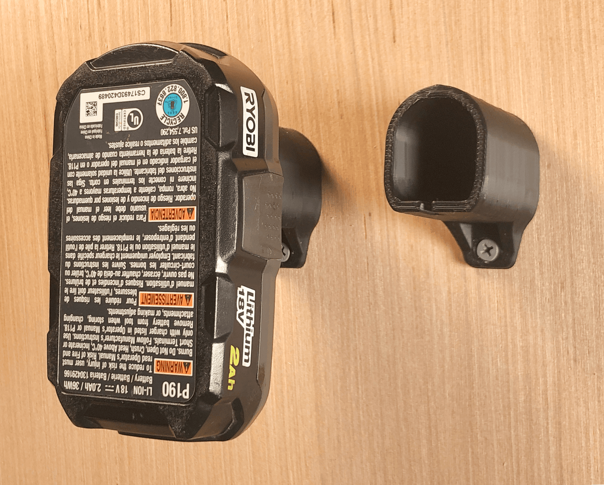 Ryobi battery stored in a black wall mount beside an empty black mount; battery and hardware are not included.